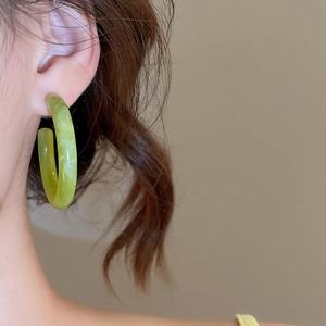 Gros plan de boucles d'oreilles en C à motif marbre vert portées par un mannequin chic