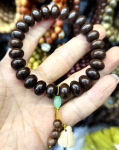 Detail of wooden beaded bracelet featuring green spacer and white lotus petal pendant