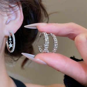 Detailed view of silver hoop earrings with pavé rhinestones and a star pendant charm