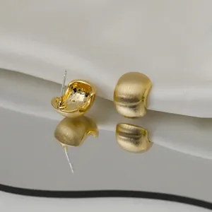 Detailed macro view of gold-finished C-shaped metal stud earrings on white silk fabric