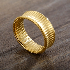 Macro detail of 18K gold plated striped ring with beaded edges on a wood surface
