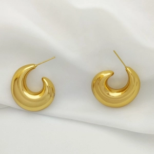 Macro shot of polished golden U-shaped earrings on soft white fabric background