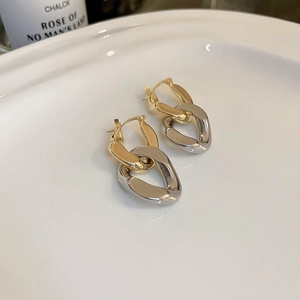 Détail de boucles d'oreilles créoles à maillons dorés et argentés sur un plat en céramique