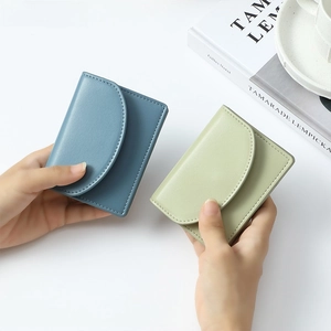 Detail of minimalist short wallets in dusty blue and green with rounded flap and stitching
