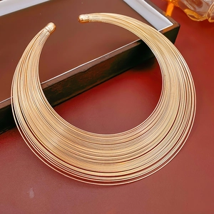 Detail eines minimalistischen, mehrlagigen Goldhalsreifs auf rotem Vintage-Lederuntergrund