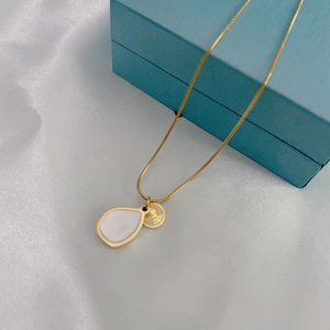 Detailed shot of golden necklace with teardrop shell pendant on silk background
