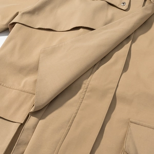 Detail of khaki trench coat featuring storm flap and double-stitched seams with metal button