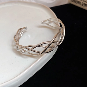 Macro view of silver woven open bangle with intricate twisted metal lines on ceramic plate