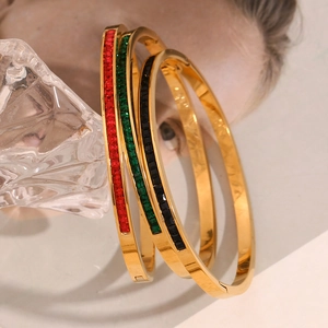 Detailaufnahme von 18K vergoldeten Armbändern mit roten, grünen und schwarzen Steinen