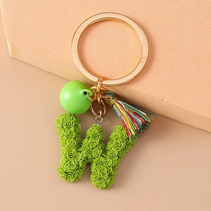 Detail of green letter W keychain with micro rose texture and colorful tassel charm