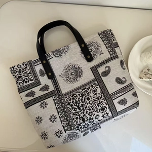Detail of vintage paisley print tote bag featuring black leather straps and rivets