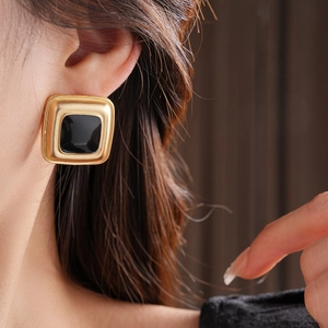 Close-up of vintage golden square earrings with black enamel inlay worn by a model