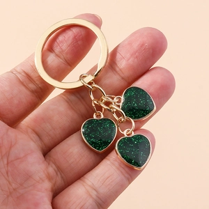 Detail of hand holding golden keychain with three green glitter resin heart charms