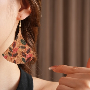 Detail of fan-shaped cork earrings with red and green leaf print on a female model