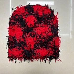 Detail of red and black distressed knit beanie with raw edge texture and frayed yarn details