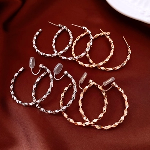 Polished silver and rose gold hoop earrings with diamond-cut texture on red silk background