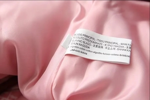 Detail view of pink cotton jacket fabric texture and multi-language material care label