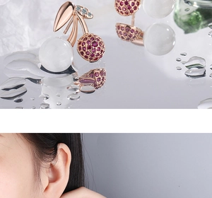 Close-up of cherry stud earrings in rose gold with red rhinestones and opal stone