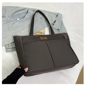 Macro view of brown nylon tote bag showing double front pockets and leather logo patch
