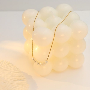Detail of 18k gold-plated chain with six white pearls on geometric candle background