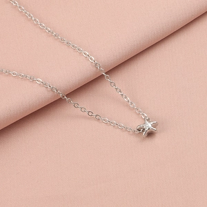 Close-up of a silver starfish pendant on a delicate chain over pink fabric