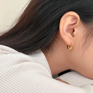 Macro shot of minimalist gold heart stud earrings worn to show modern polished finish