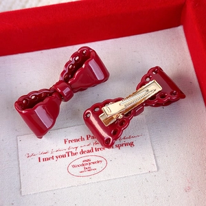 Detail showing red hollow bow hairpins with gold metal duckbill clips on a gift box
