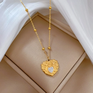 Detail of a gold heart pendant with white crystals in a beige jewelry box with soft fabric