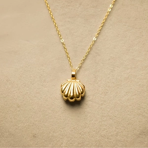 Vintage golden shell locket necklace with faux pearl on a textured beige background
