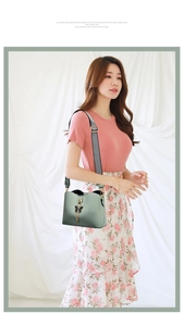 Green shoulder bag with bow metal clasp and black-white woven strap worn by a model