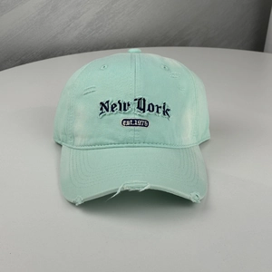 Detail der mintgrünen Vintage-Baseballkappe mit New York-Stickerei und Riss am Schirm