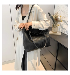 Detail of a large black leather woven tote bag carried by a model in a minimalist setting