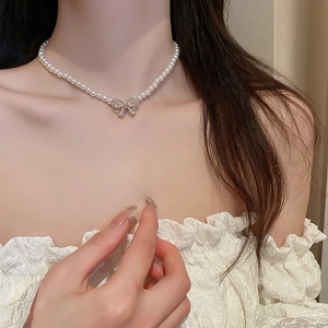 Close-up of elegant bow pendant with rhinestones on a white pearl necklace worn by a model