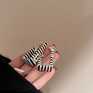 Detail of square faux leather earrings featuring black and white stripes and gold letter B