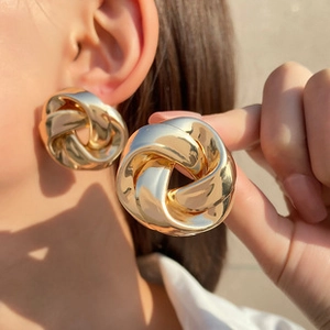 Close-up of chunky gold C-shape twisted metal hoop earrings with a polished finish