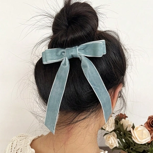 Elegant grey-blue velvet bow hair clip with long ribbons shown on a bun hairstyle