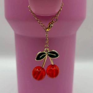Detail of a cherry pendant with red resin fruit and green leaves on a golden chain