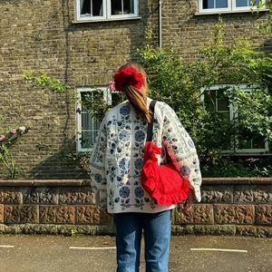 Detail of white quilted jacket with blue floral embroidery and a red ruffled crossbody bag