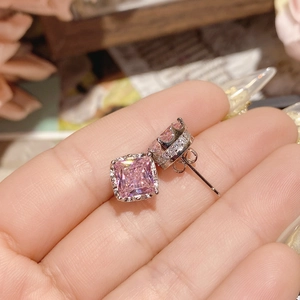 Macro detail of pink square-cut gemstone earrings with white zircon halo on palm