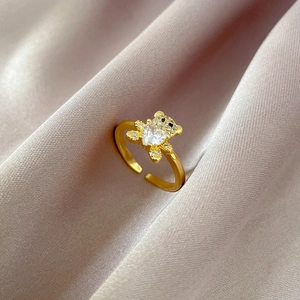 Detailed close-up of gold bear-shaped open ring with heart-shaped diamond on pink silk