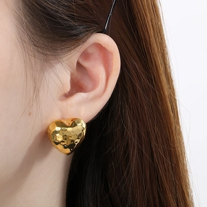 Polished gold heart-shaped stud earrings with hammer-textured finish worn by a model