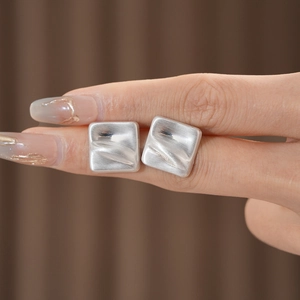 Detail of matte silver square stud earrings with textured brushed metal finish and waves