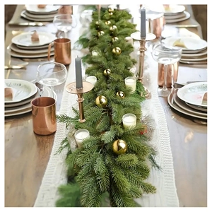 Macro shot of realistic PE pine needle garland with gold baubles and white candles