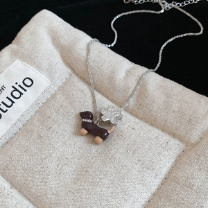 Vue rapprochée du pendentif teckel et fleur en argent sur un sac en tissu rustique