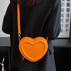 Dettaglio di una borsa a cuore arancione vivace con texture a rilievo e blazer nero