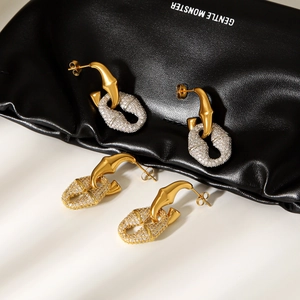 Detailed interlocking gold and silver earrings with pavé diamonds on a leather surface