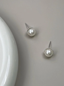 Macro detail of elegant pearl earrings with silver textured metal base on grey backdrop