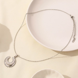 Close-up of silver moon pendant necklace with pavé zircon stones on a white ceramic plate