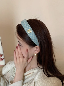 Dettaglio del cerchietto in tweed azzurro con logo dorato indossato da modella