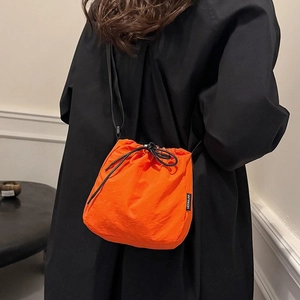 Vibrant orange drawstring bucket bag with black strap worn over a black winter coat
